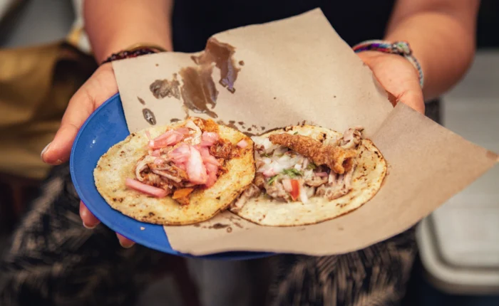 Host holding a blue plate with two cochinita tacos and pickled onions