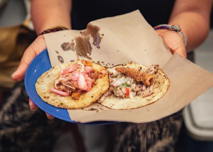 Host holding a blue plate with two cochinita tacos and pickled onions